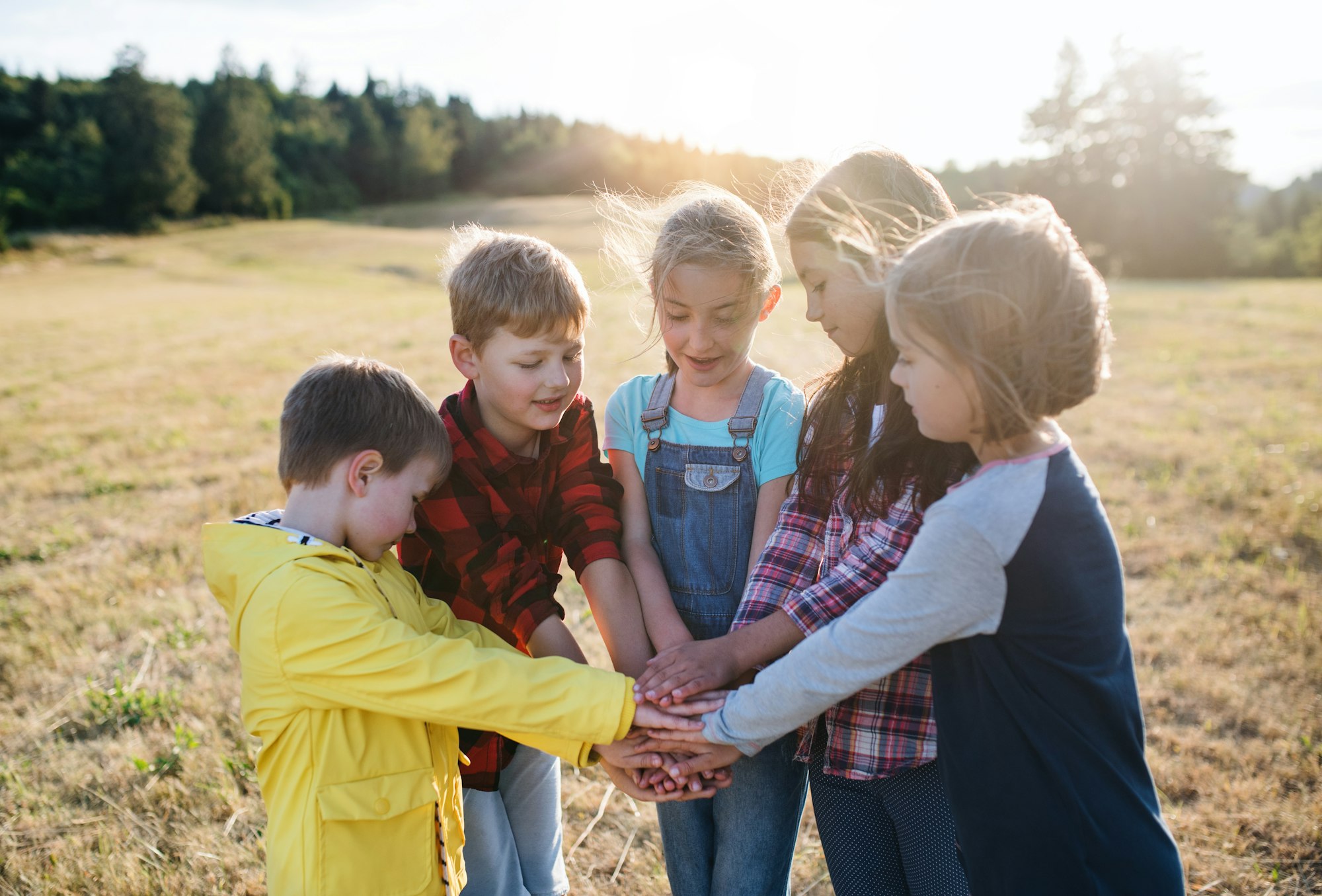 Group of school children standing on field trip in nature, putting hands together